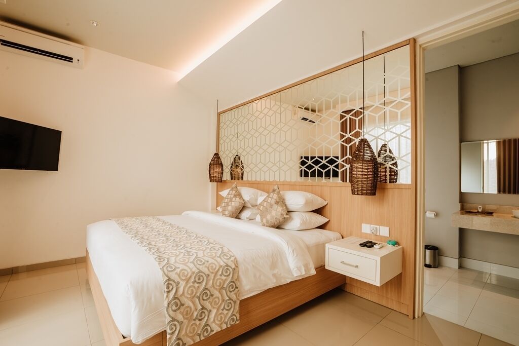 Un dormitorio moderno con una cama de madera, una mesita de noche, un televisor montado en la pared y un baño con espejo y lavabo.