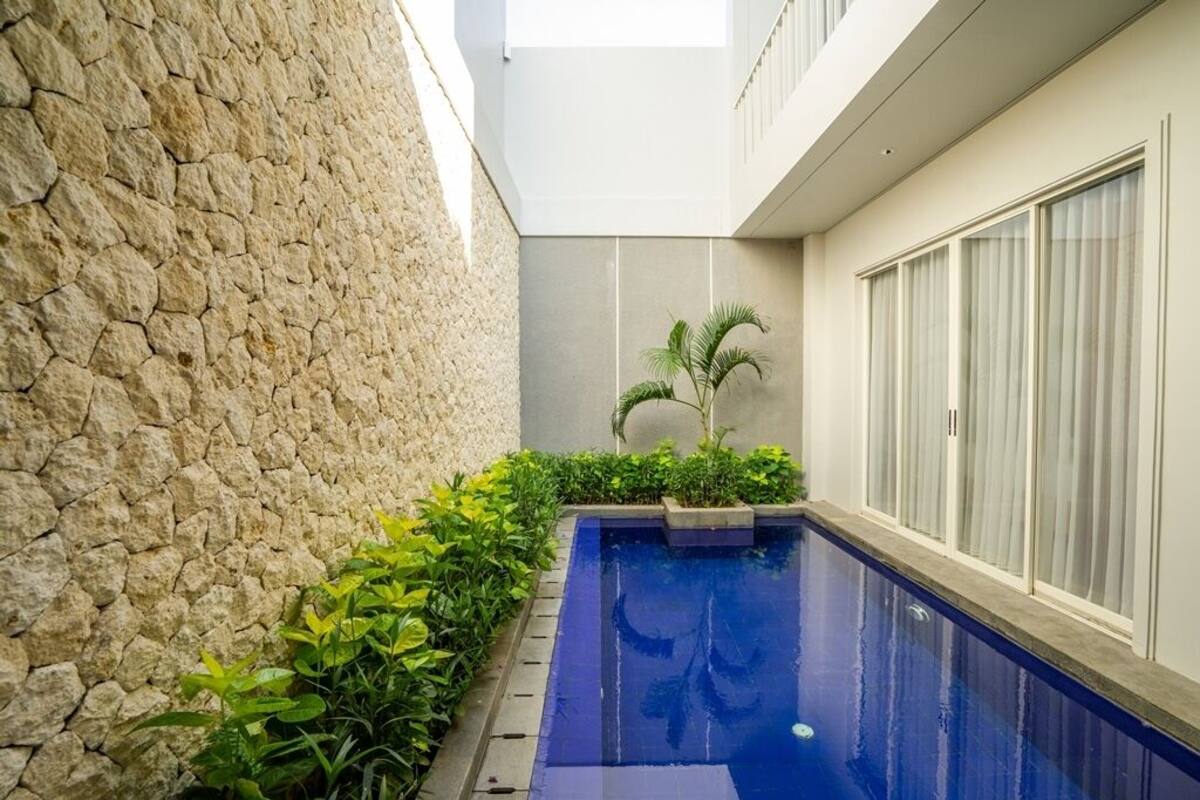 A modern pool area with a stone wall, a small garden with plants, and a large window with blinds.