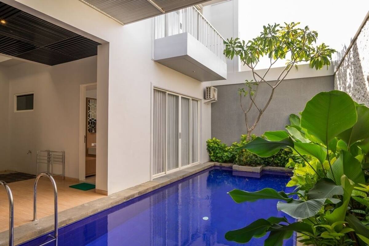 A modern outdoor pool area with a clear blue pool, a small deck, and surrounding greenery.