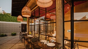 An outdoor dining area with tables and chairs, large wicker pendant lights, and a view of the surrounding landscape.