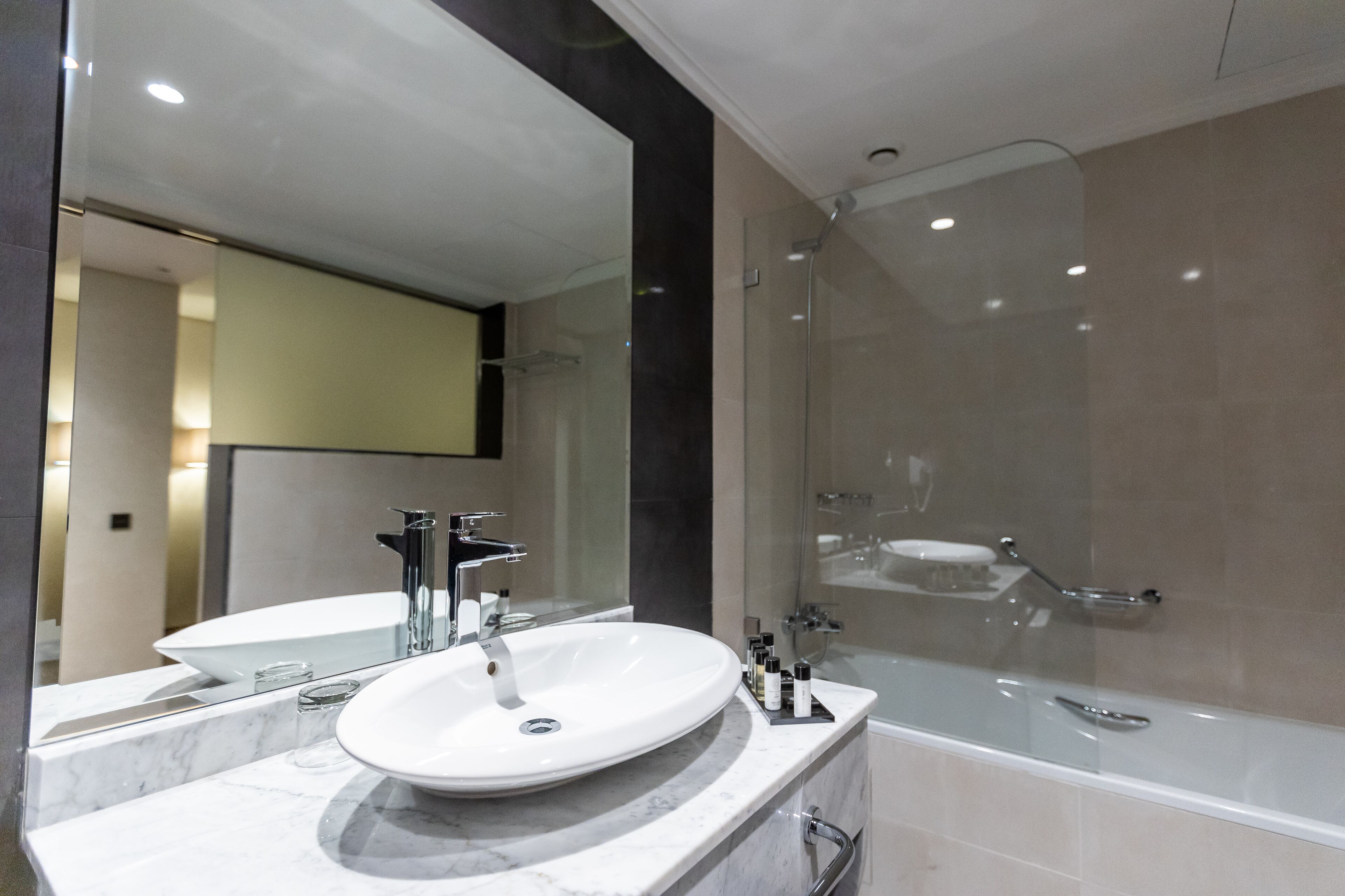 A modern bathroom with a white sink, a large mirror, and a glass-enclosed shower.