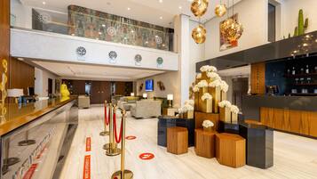 A modern hotel lobby with a reception desk, seating area, and a bar.