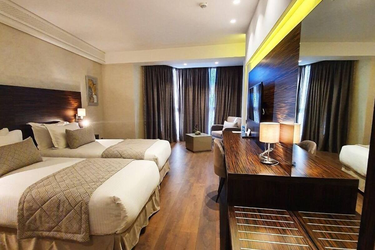 A hotel room with two beds, a desk, a chair, and a large mirror.