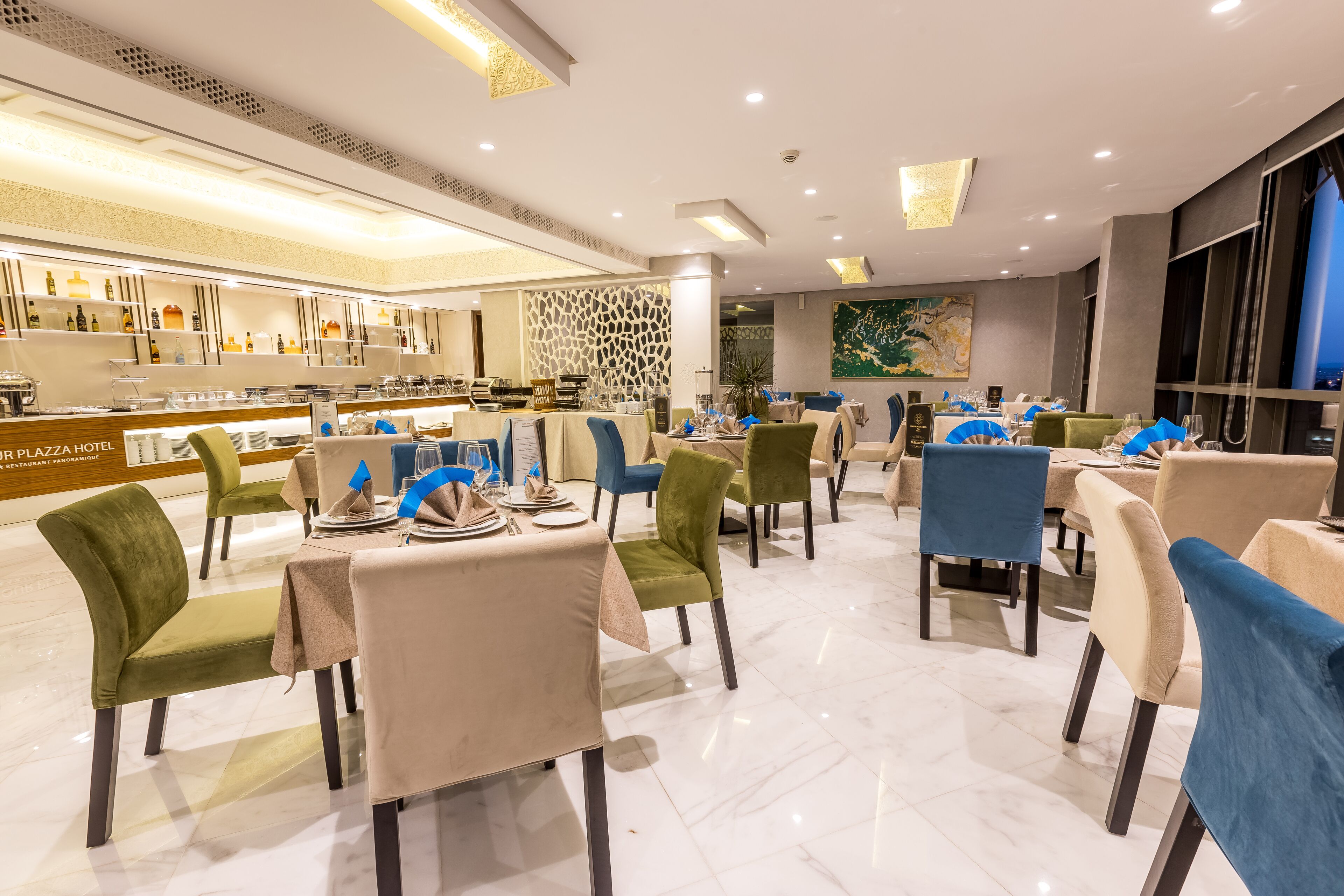 A modern restaurant with a bar area, green and blue chairs, and a polished marble floor.