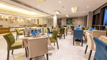 A modern restaurant with a bar area, green and blue chairs, and a polished marble floor.