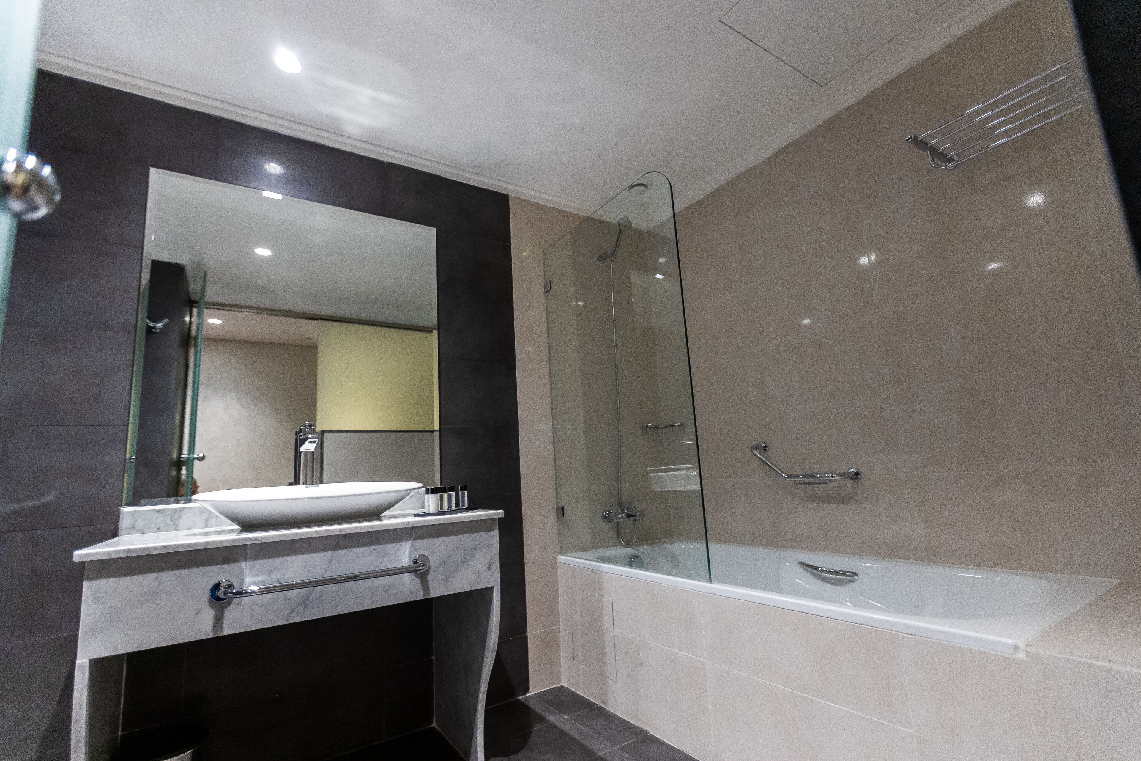 Un baño moderno con ducha envuelta en vidrio, una bañera blanca y un tocador de mármol con lavamanos.