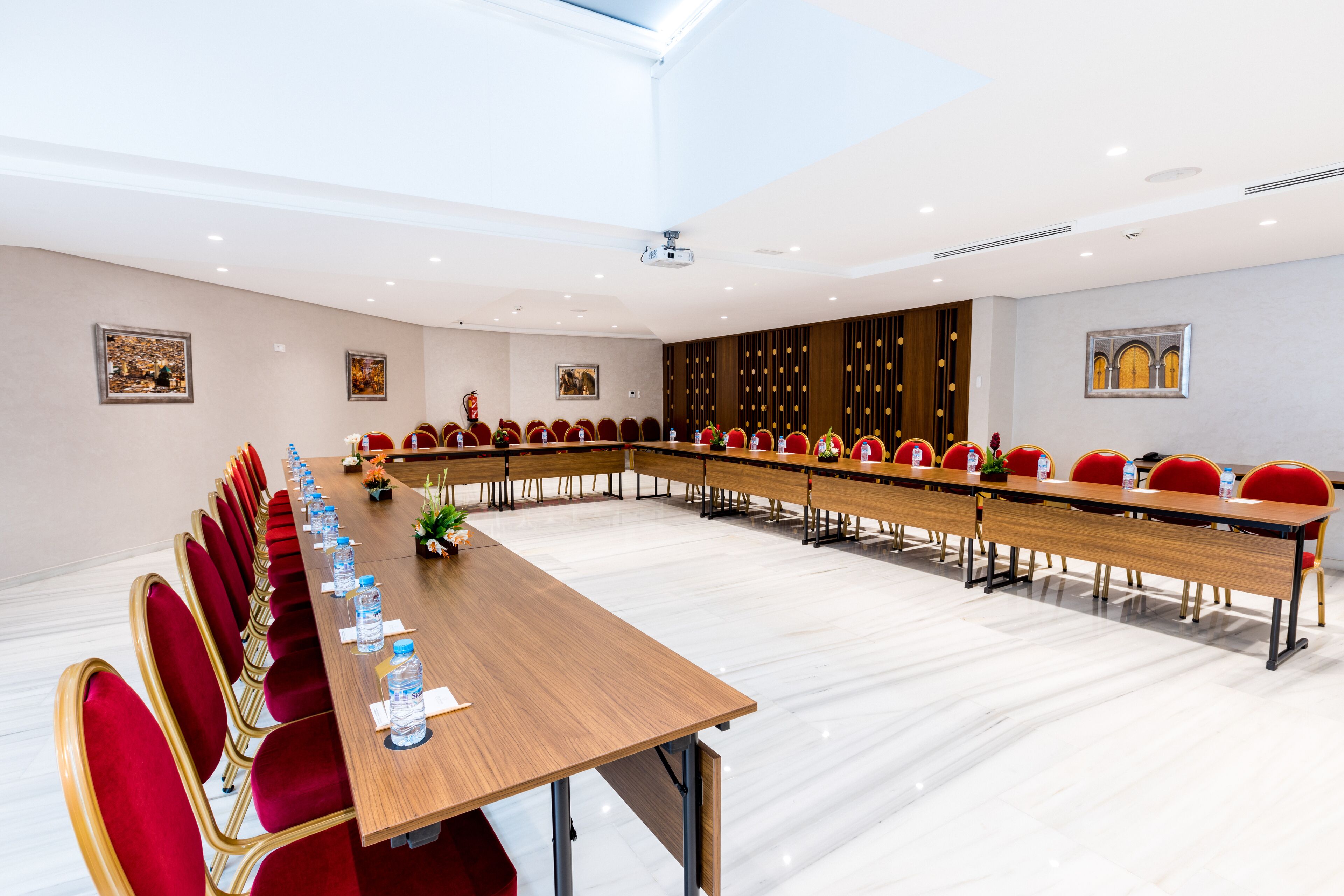 Une salle de conférence avec une longue table, des chaises rouges et un écran de projection.