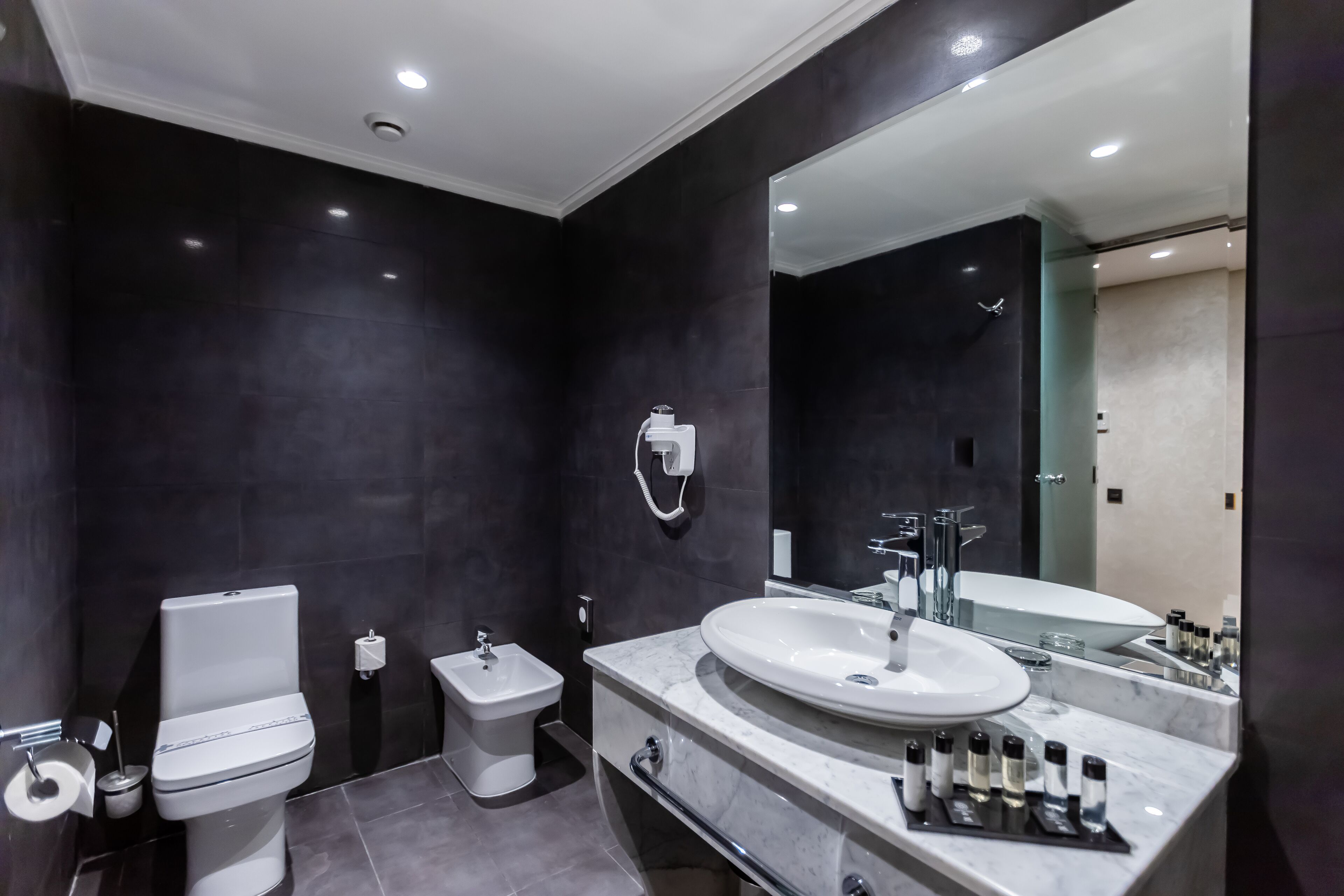 Een moderne badkamer met toilet, bidet, wastafelmeubel met grote spiegel en wastafel.