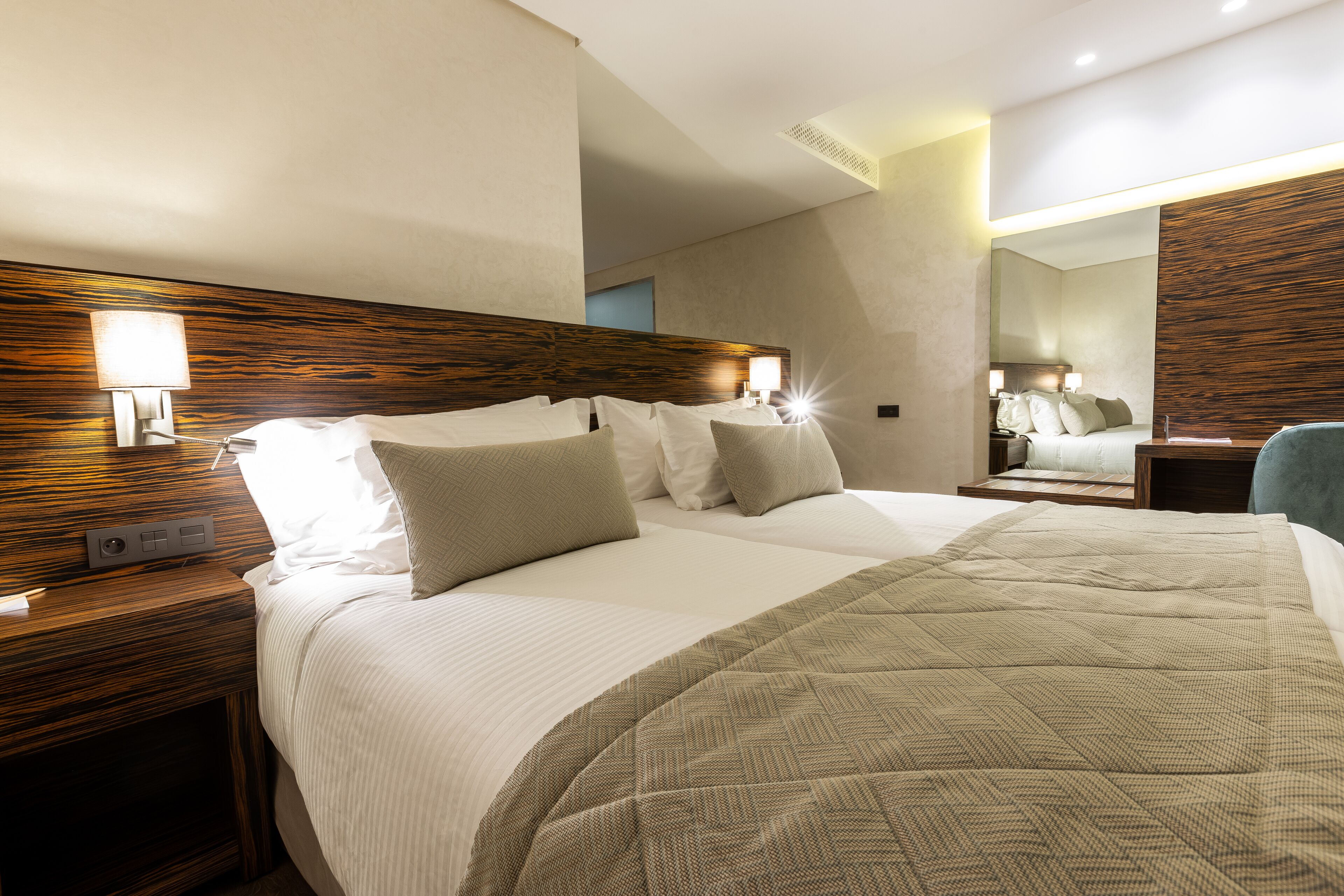 Une chambre d’hôtel avec un grand lit, une tête de lit en bois, des lampes de chevet et un miroir.