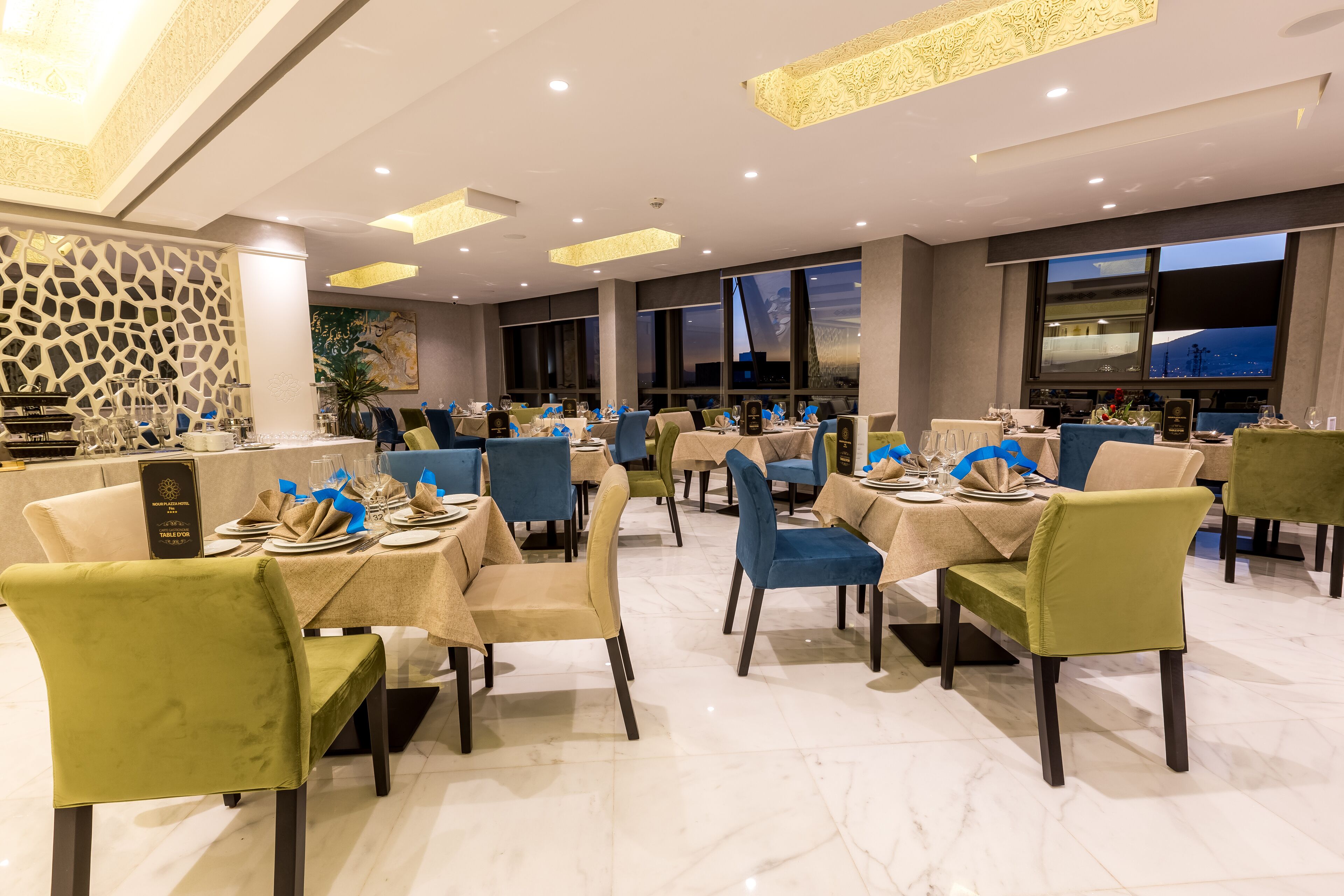 Un restaurante con varias mesas dispuestas para comer, que presenta un interior moderno con piso de mármol y mobiliario contemporáneo.