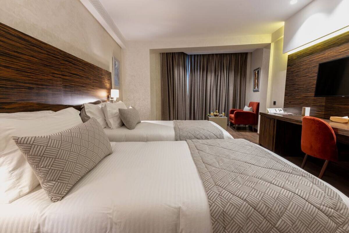 A hotel room with two beds, a desk, a TV, and a red chair.
