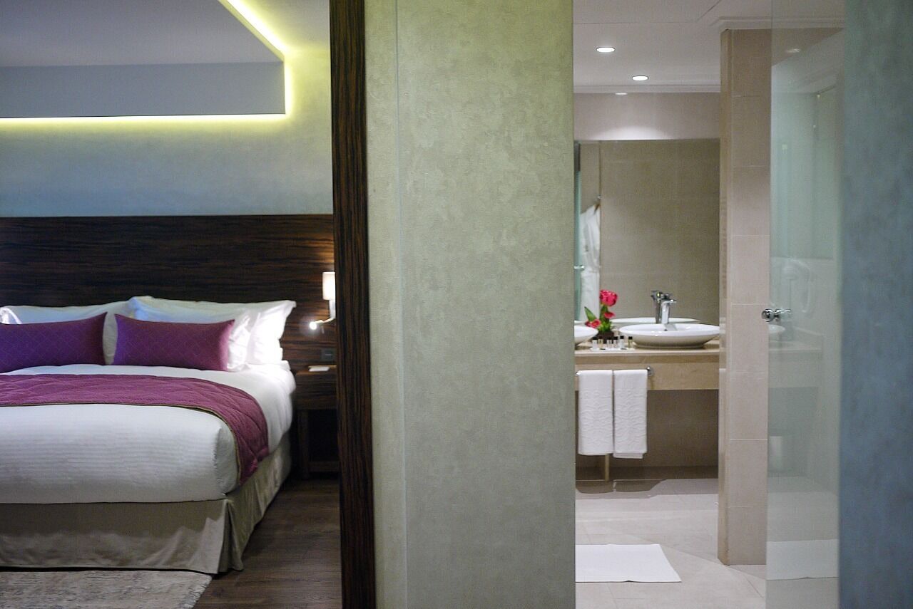 A modern hotel room with a bed, bedside table, and a bathroom visible through an open door.