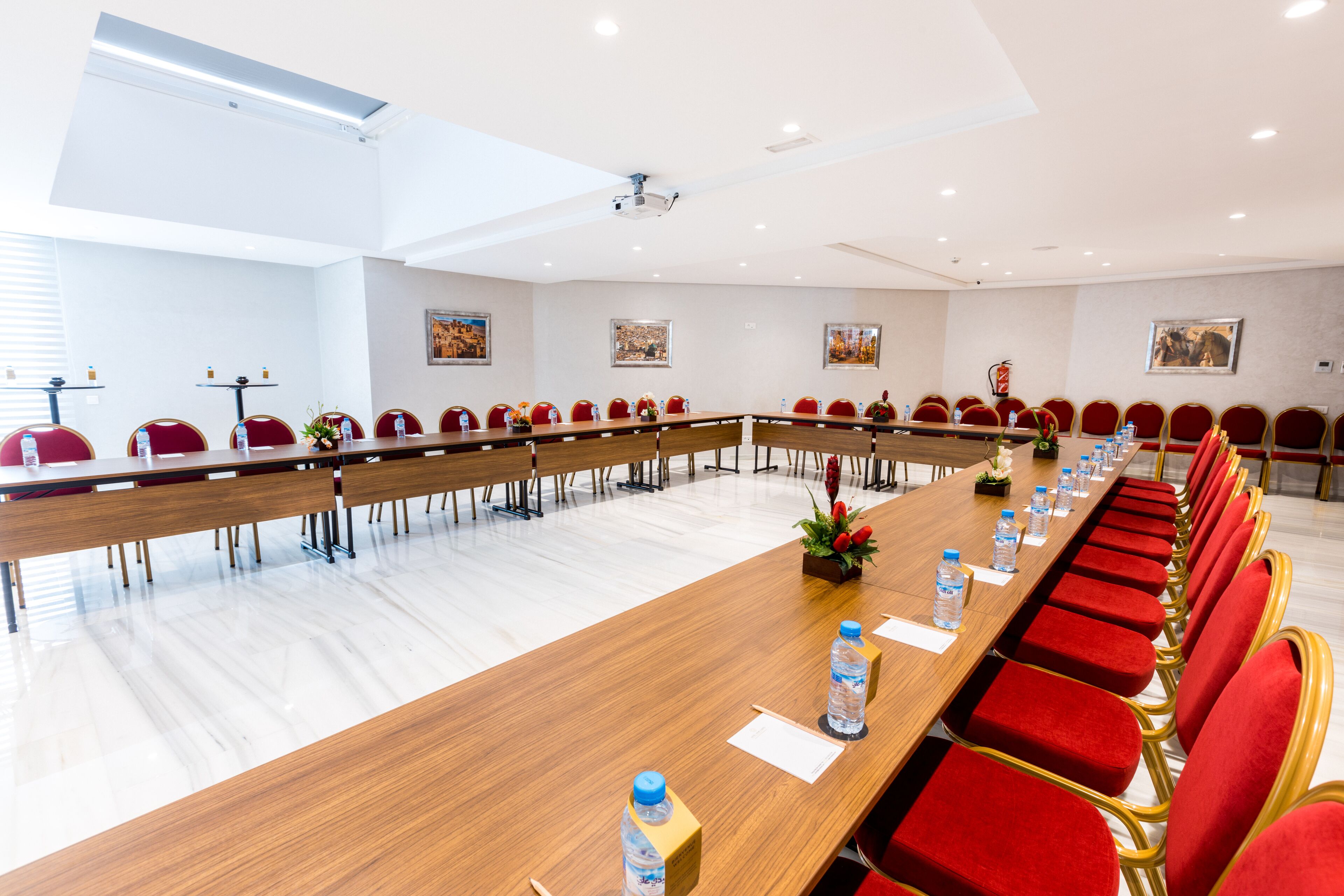 Una sala de conferencias con una larga mesa, sillas rojas y botellas de agua.