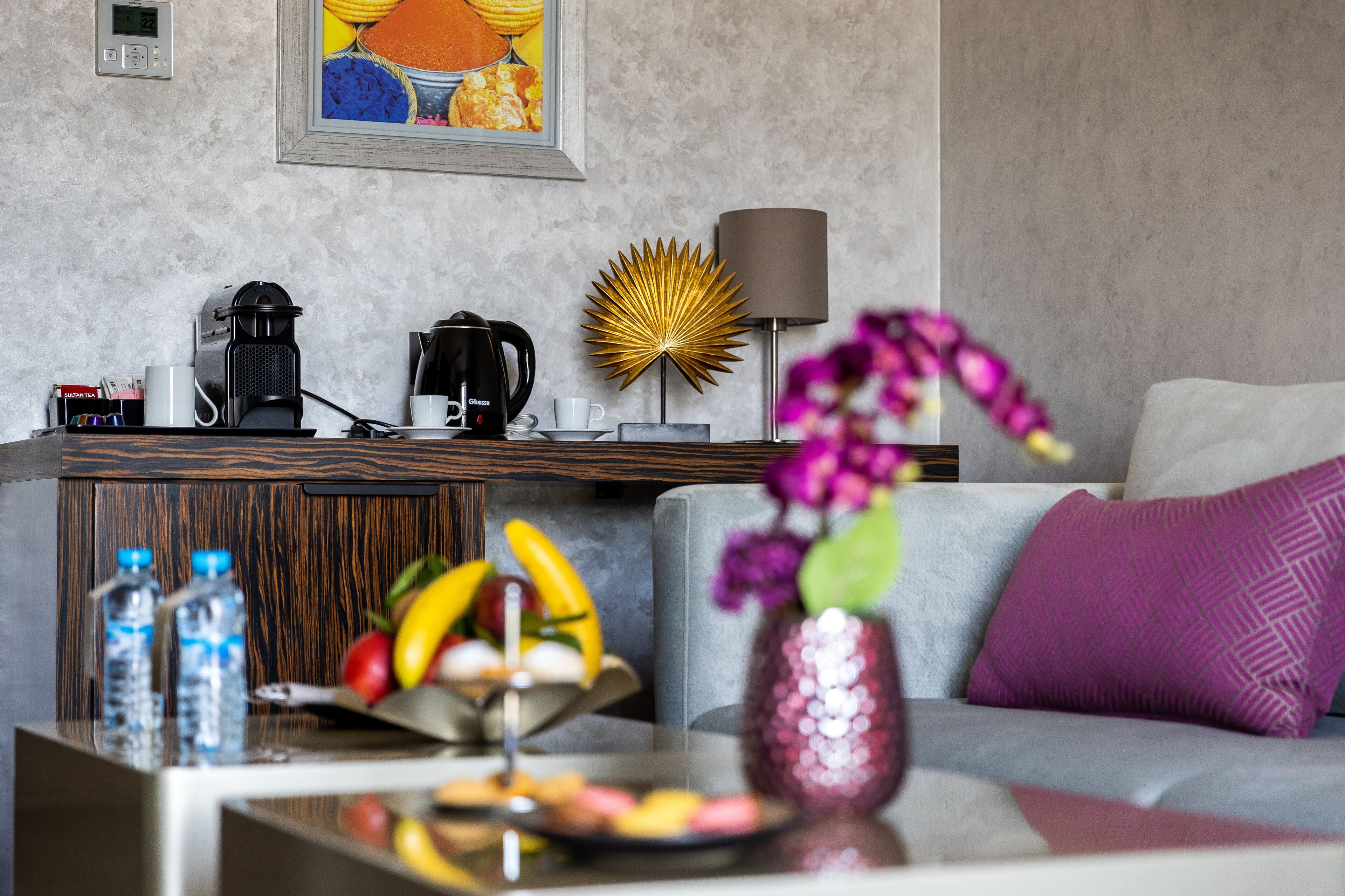 A modern living room with a coffee maker, a lamp, and a fruit bowl on a glass table.