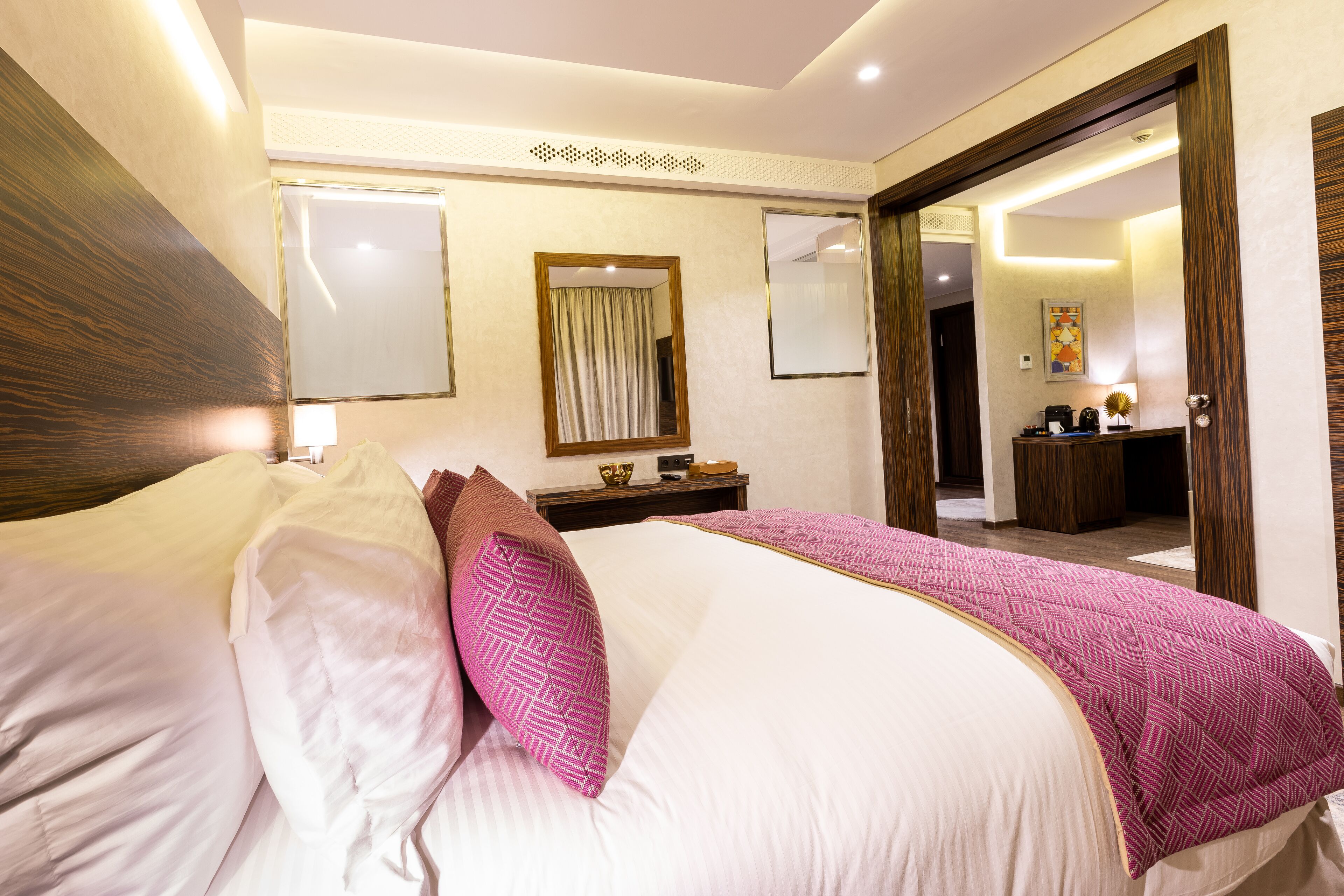 Une chambre d’hôtel avec un grand lit, une tête de lit en bois, une table de chevet avec une lampe et un miroir au mur.