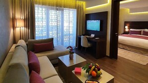 A modern hotel room with a sofa, a coffee table with fruit, a desk with a computer, and a TV. - Nour Plazza Fes (Fes)