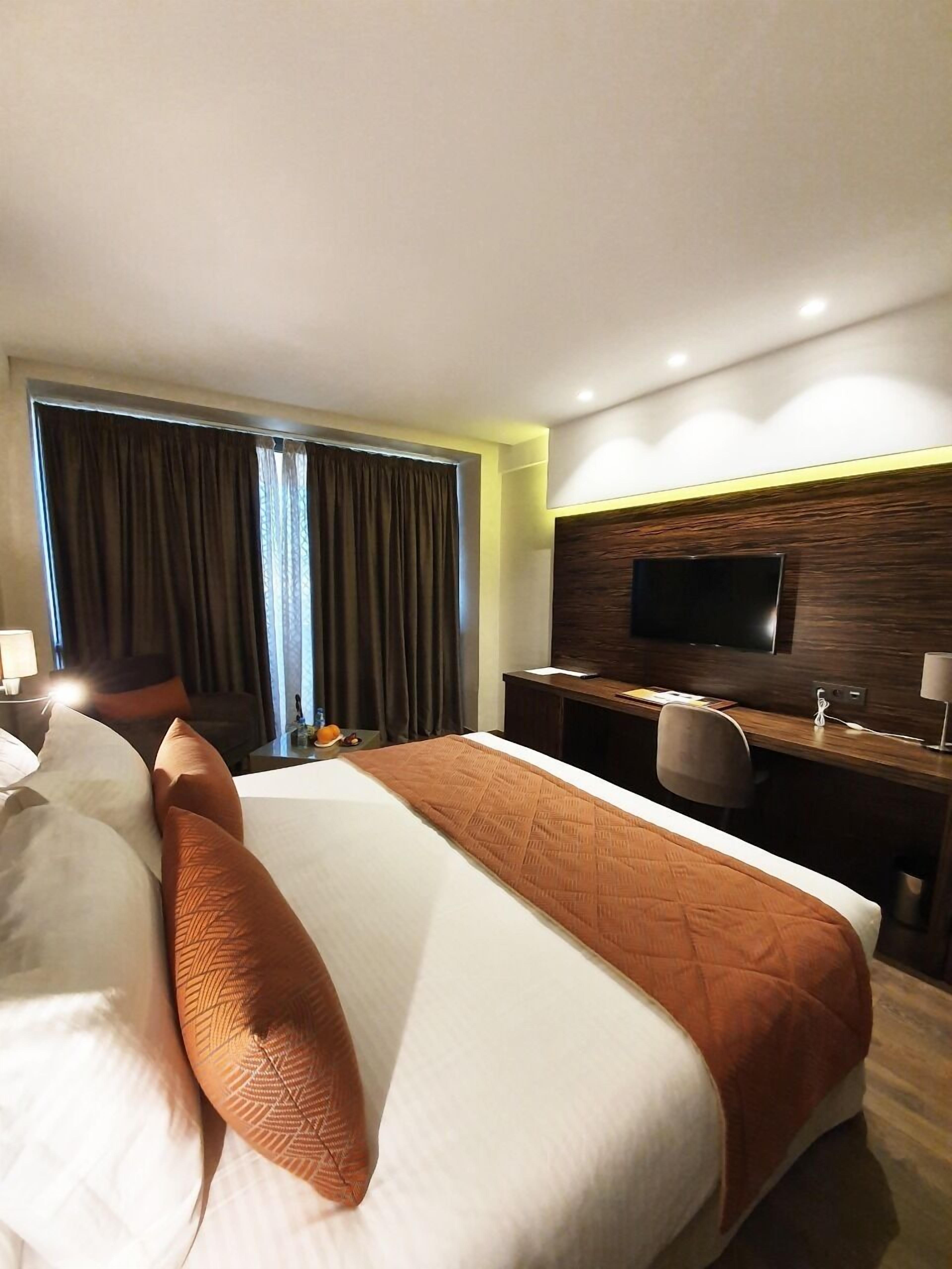 Ein Hotelzimmer mit Bett, Schreibtisch, Fernseher und einem Fenster mit Vorhängen.