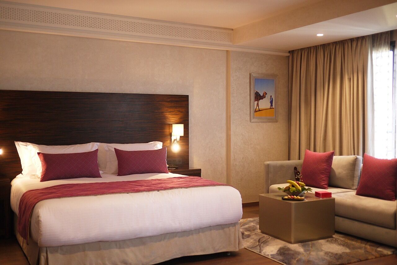 Ein Hotelzimmer mit einem großen Bett, einer Couch, einem Couchtisch mit Obst und einem Gemälde an der Wand.