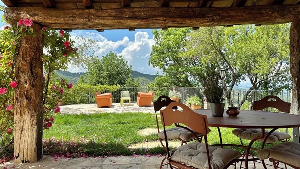 Un patio al aire libre con una mesa y sillas, rodeado de vegetación y vistas al paisaje.