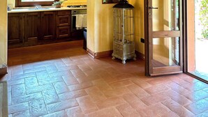 Una cocina rústica con vigas de madera, suelo de baldosas de piedra y vistas a través de un ventanal abierto.