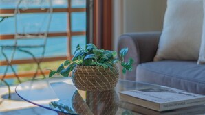 A living room with a glass table, a wicker plant, a book, and a view of the outdoors.