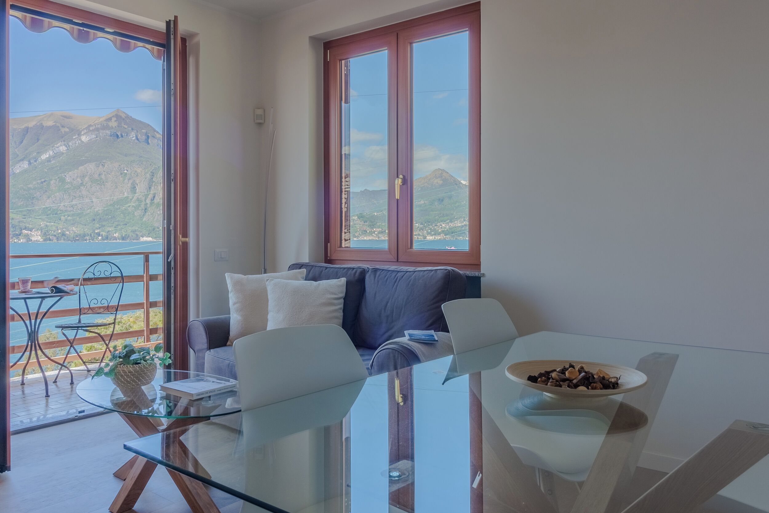 Un soggiorno moderno con un tavolo in vetro, un divano e vista sul mare e sulle montagne.