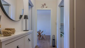 A hallway with a white dresser, a mirror, a lamp, and a dining area with a table and chairs.