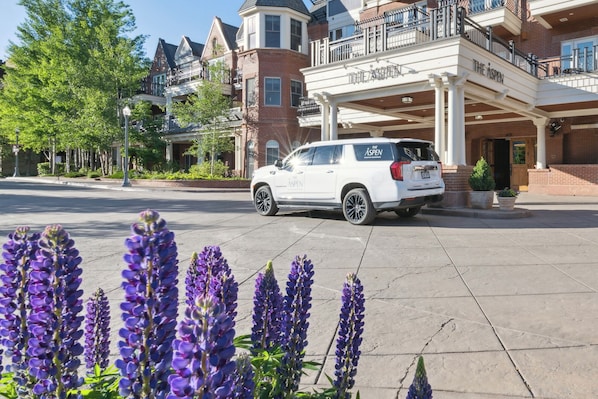 A white SUV parked in front of a hotel with a balcony and a sign that reads "The Aspen".