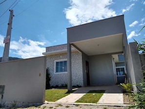 Uma casa moderna de dois andares com varanda coberta, pequeno jardim frontal e janela visível.