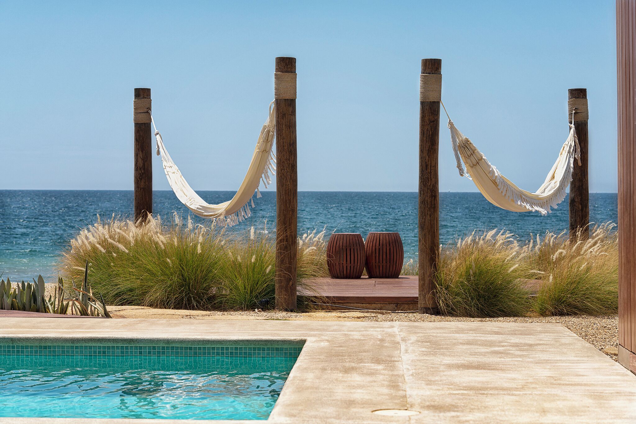 A pool area with a hammock, wooden posts, and a view of the ocean.