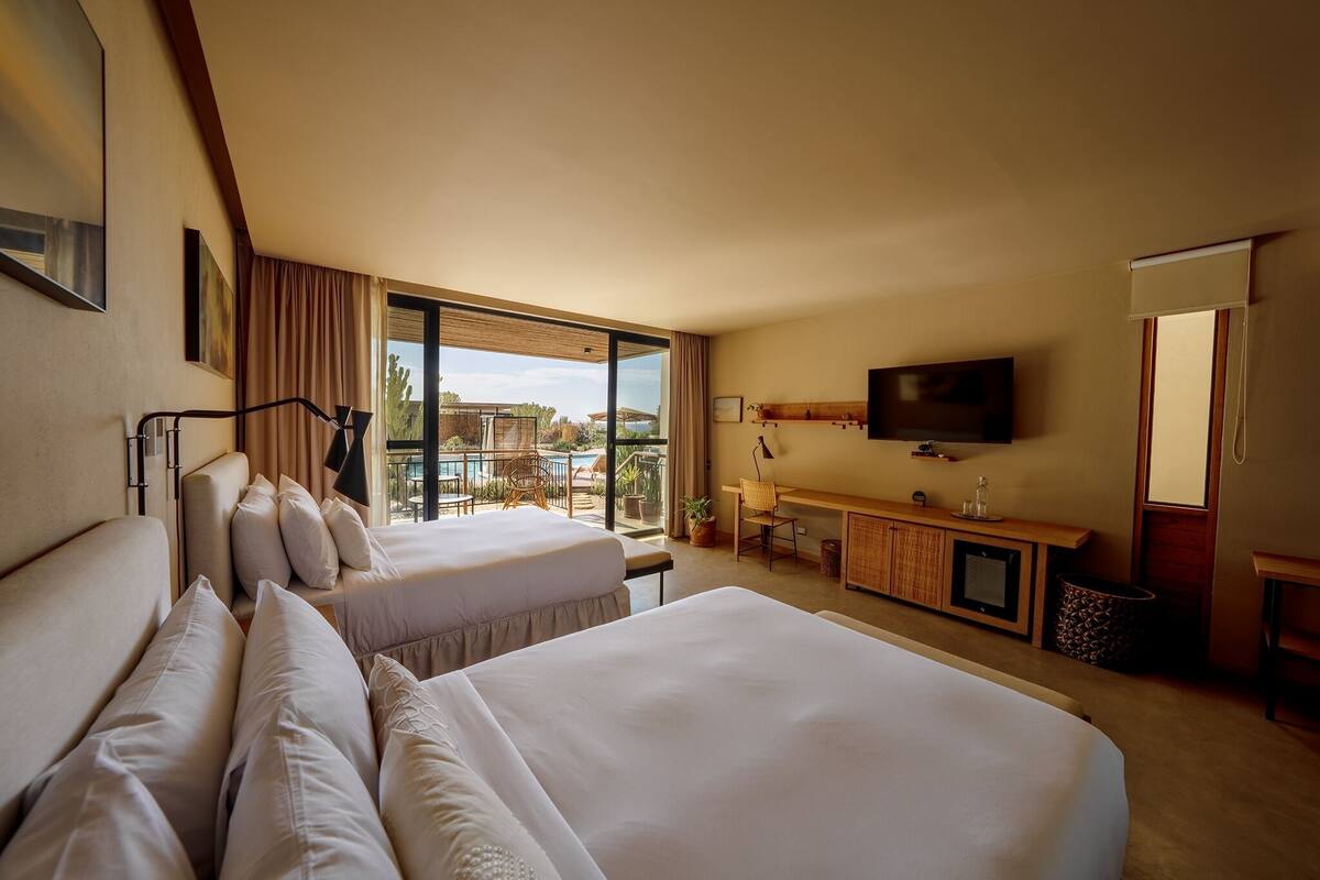Habitación de hotel con dos camas, un escritorio, un televisor y un balcón con vista a la piscina.