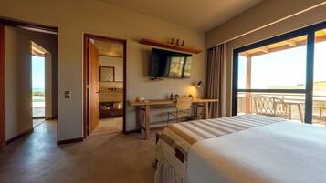 Quarto de hotel com cama, escrivaninha, cadeira, televisão e varanda com vista.