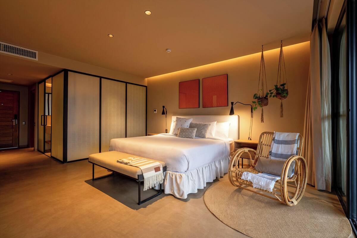 Un dormitorio moderno con una cama grande, un banco, una mecedora y vistas al exterior.