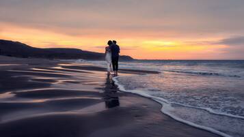 A beach scene with a couple walking along the shore during sunset.