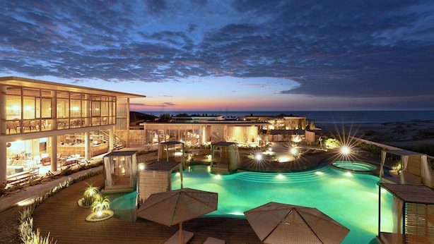 A resort with a swimming pool, outdoor seating, and a view of the ocean at dusk.