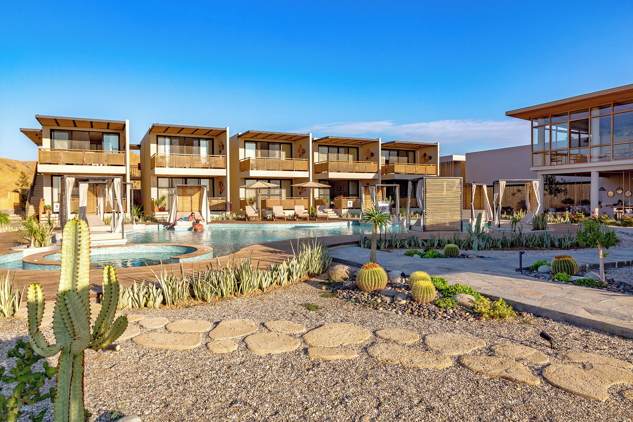 Un resort con edificios de varios pisos, piscina y jardines desérticos con cactus y rocas.