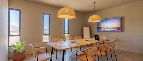 A spacious dining area with a long table, wicker chairs, and pendant lights.