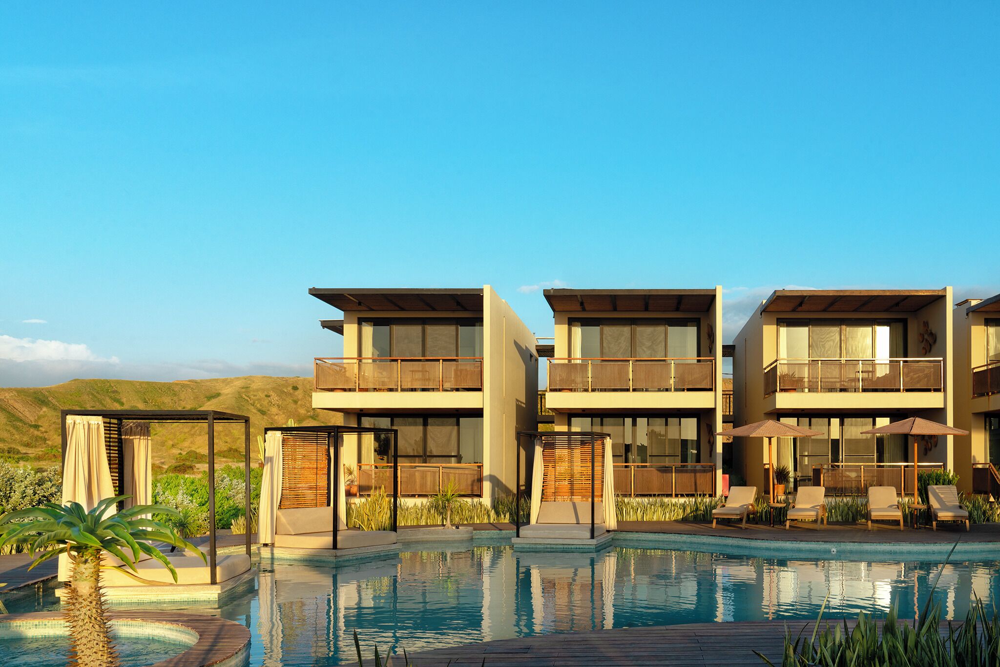 A modern hotel with a pool, multiple balconies, and a desert landscape in the background.