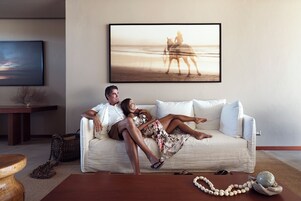 Una pareja descansando en un sofá blanco en una sala de estar con un cuadro de una escena de playa en la pared.
