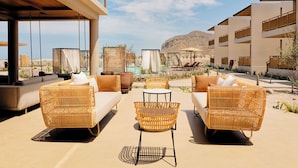A modern outdoor lounge area with wicker furniture, a round table, and a view of the desert landscape.