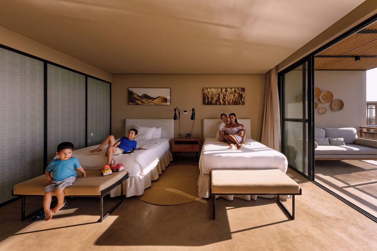 Una habitación de hotel moderna con dos camas, un sofá y un gran ventanal corredero al balcón.