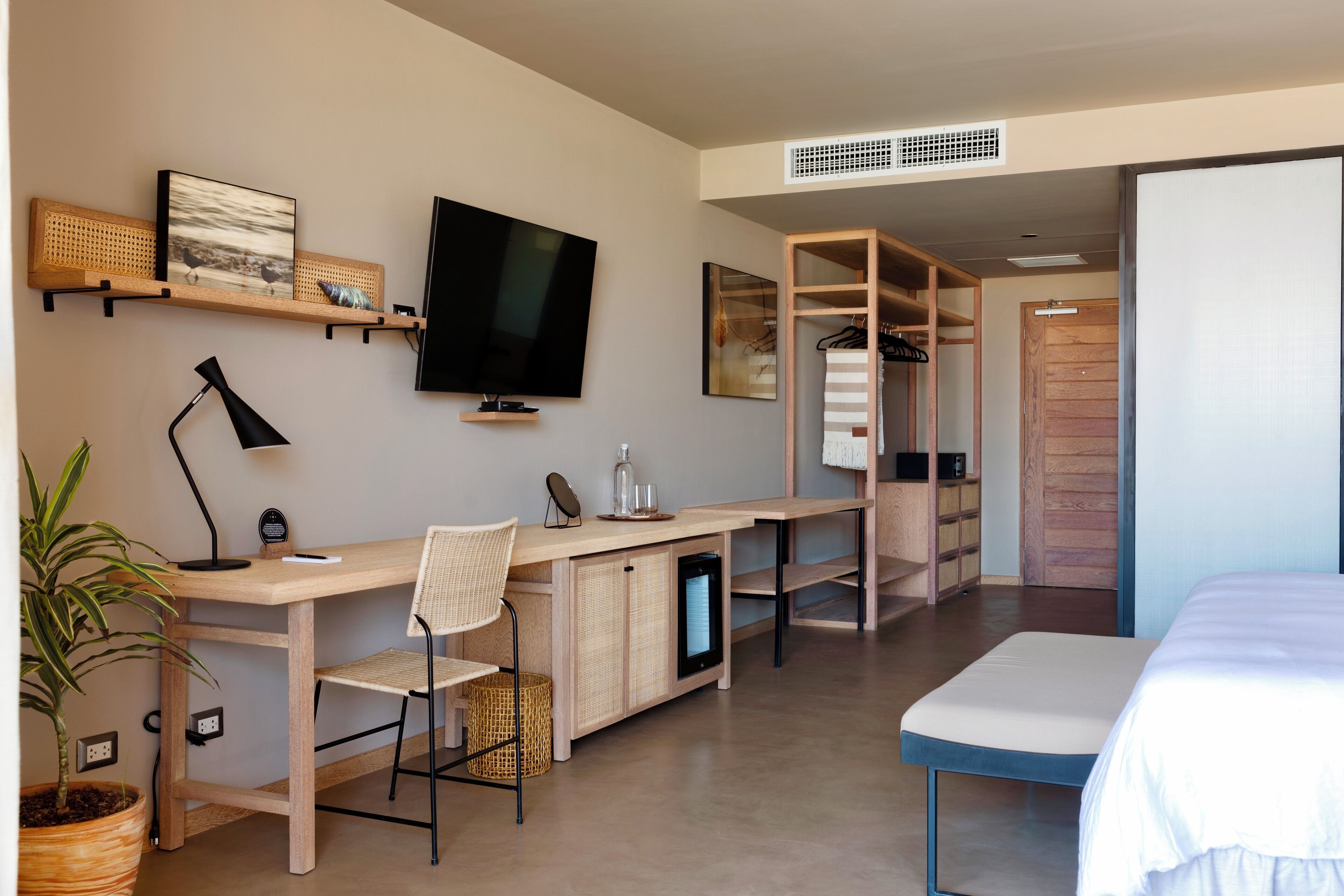 A modern hotel room with a wooden desk, a flat-screen TV, a bed, and a walk-in closet.