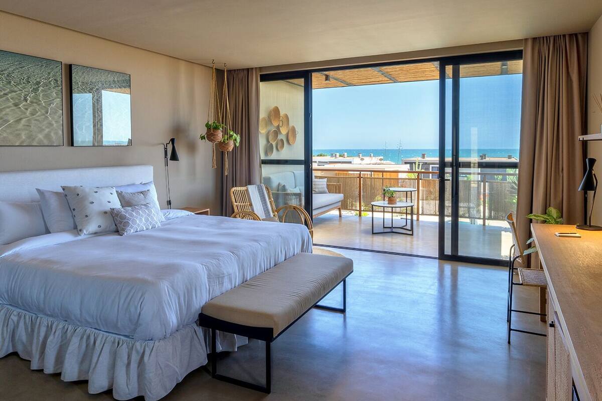 Un dormitorio amplio con una cama grande, un banco y un balcón con vistas al mar.