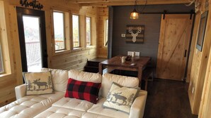 L’intérieur chaleureux d’un chalet avec un grand canapé confortable, une table à manger et un mur en bois orné d’une tête de cerf.
