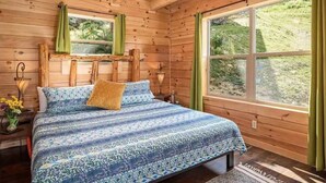 Une chambre dans une cabane en bois, avec un lit, deux fenêtres et une vue sur la verdure.