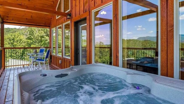 Une terrasse en bois dotée d’un jacuzzi, de coins salon extérieurs et de grandes fenêtres offrant une vue sur le paysage.