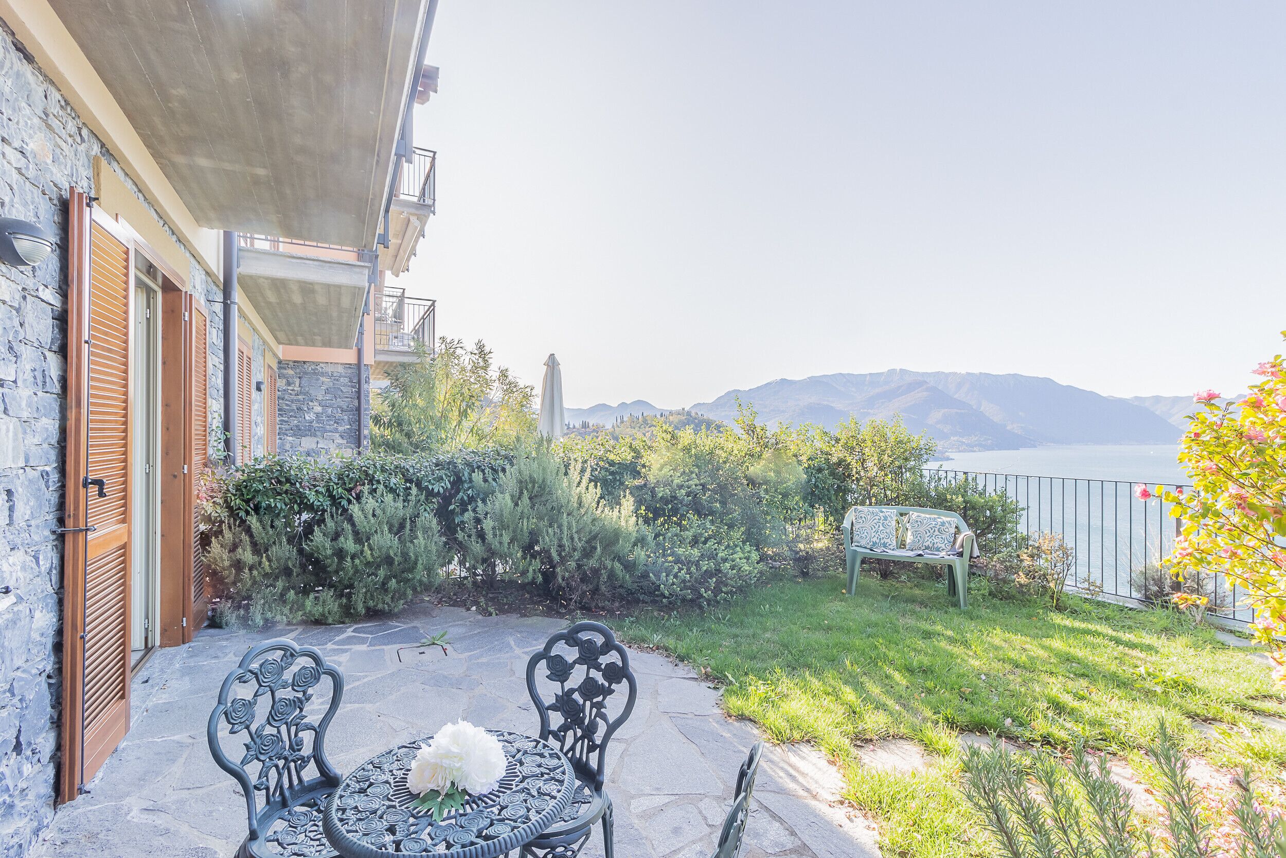 A patio with a table and chairs, a white dog, and a view of mountains and water.