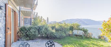 A patio with a table and chairs, a white dog, and a view of mountains and water.