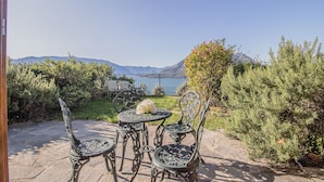 Un área de estar al aire libre con una mesa, sillas, un arreglo floral y vistas a un lago y montañas al fondo.