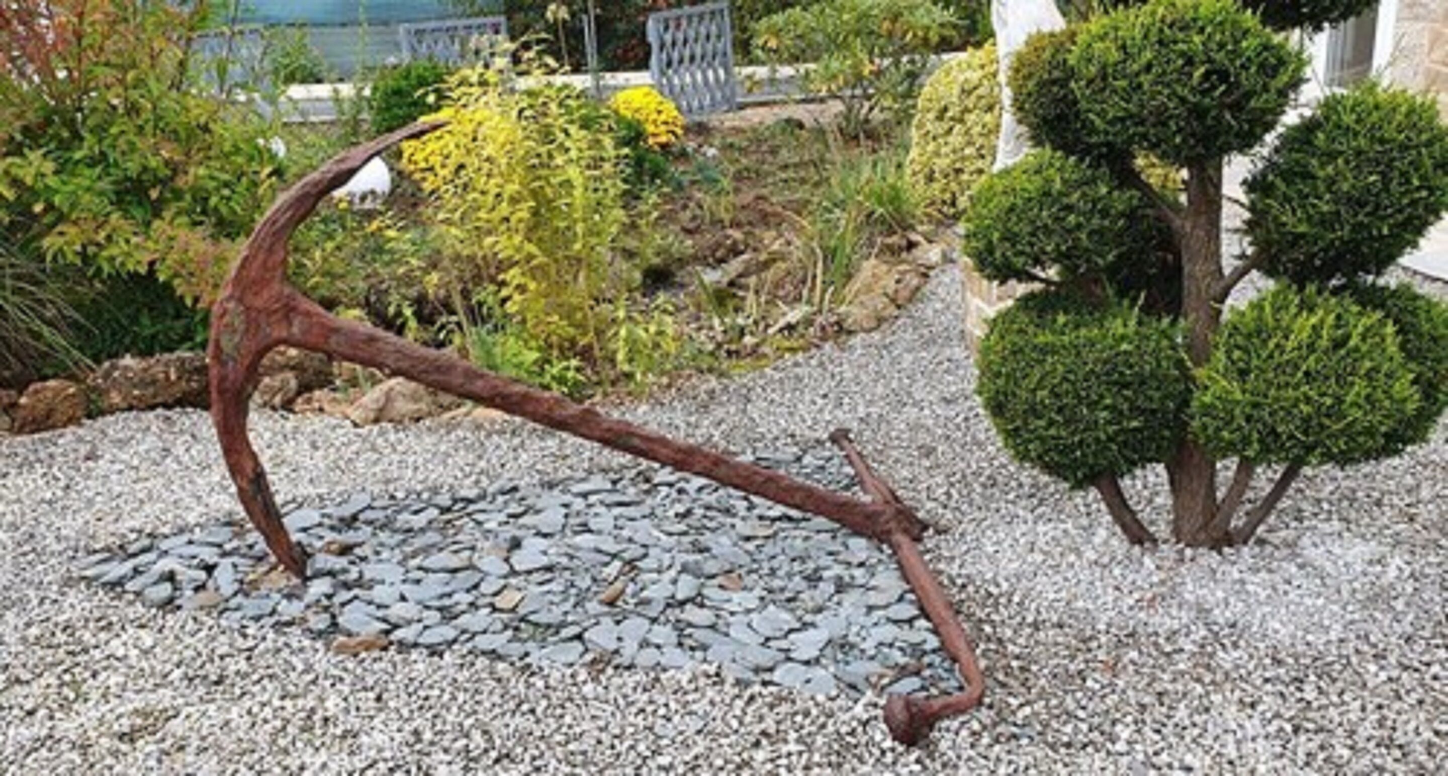 A garden with a gravel path, a metal sculpture, and neatly trimmed bushes.